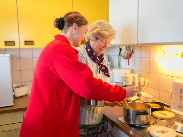 Pflegerin hilft die Seniorin beim kochen